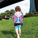Little child walking on grass wearing a striped shirt and blue patterned leggings, carrying a pink and blue butterfly backpack.
