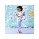 Little girl with curly hair wearing a striped sweater and holding a water bottle, standing with a Skip Hop Narwhal backpack.