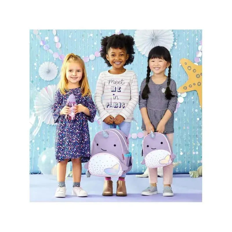 Three children stand together, smiling, each wearing a Skip Hop Narwhal backpack, with a cheerful backdrop.