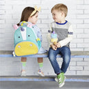 Little girl with a unicorn-themed Skip Hop backpack sits on a bench, smiling at a boy holding an ice cream cone.