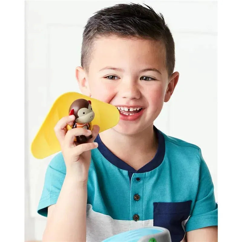 Child holding a monkey toy from the Skip Hop Zoo Outdoor Adventure Playset, smiling while wearing a blue striped shirt.