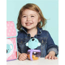 A smiling young girl holds a Skip Hop Zoo Snack Cup shaped like a koala, filled with snacks, next to a matching pink bag.