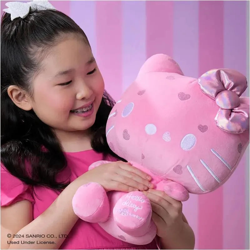 A young girl in a pink dress happily holds a large, soft pink Hello Kitty plush toy with a bow.