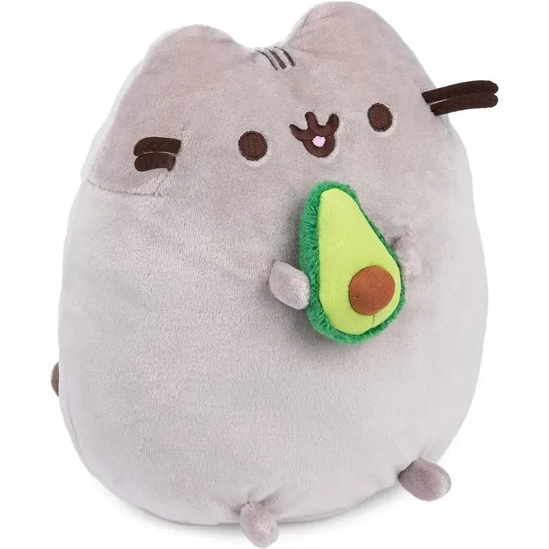 Gray plush toy of Pusheen holding a green avocado with a brown pit, suitable for ages 8 and up.
