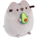 Gray plush toy of Pusheen holding a green avocado with a brown pit, suitable for ages 8 and up.