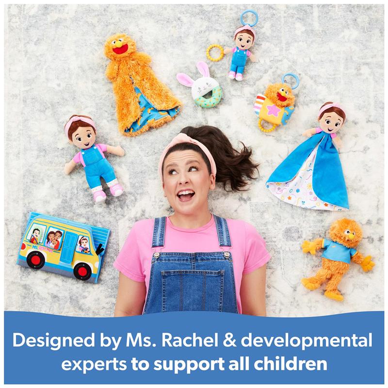 Ms. Rachel smiling on a gray surface surrounded by colorful toys and a book, promoting her Herbie Huggable Security Blankets.
