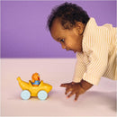 Baby reaching for a yellow toy vehicle with a pull-along design and a click-in figure smiling from the seat.