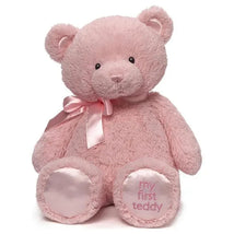 Pink plush teddy bear with a satin ribbon, featuring “my first teddy” embroidered on its foot.