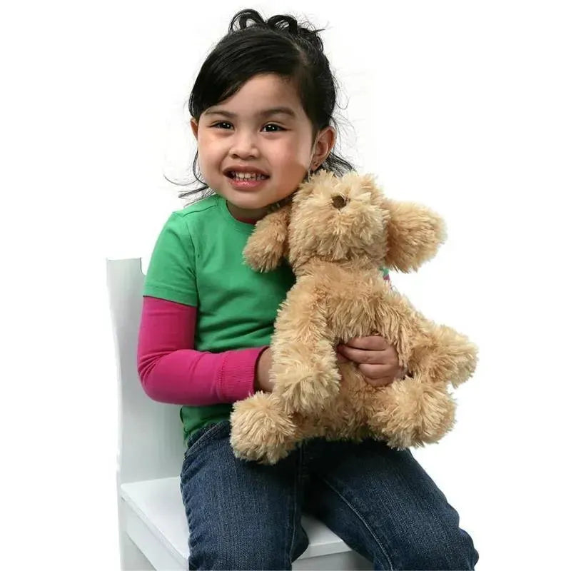 Young girl with dark hair smiles while holding a soft, tan plush cockapoo puppy. She wears a green shirt and blue jeans.