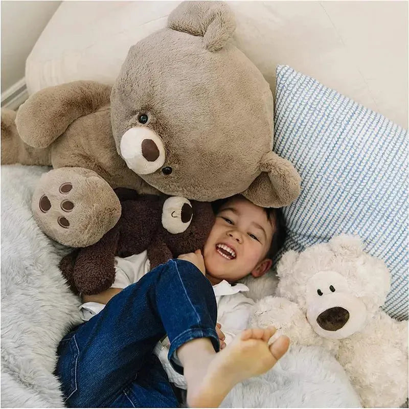 A child happily cuddles with multiple plush bears, including a large beige Philbin plush toy, on a cozy surface.