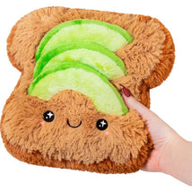 Plush avocado toast toy with a smiling face, featuring green avocado slices on brown bread, held in a hand.