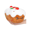 Mini Comfort Food Fruitcake plush toy with a smiling face, topped with red cherries and green candy, held in a hand.