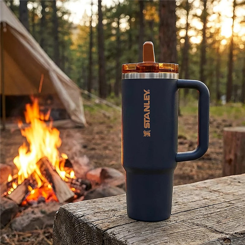 Stanley The Quencher ProTour Flip Straw Tumbler 30 oz in navy blue with orange lid, displayed outdoors by a campfire.