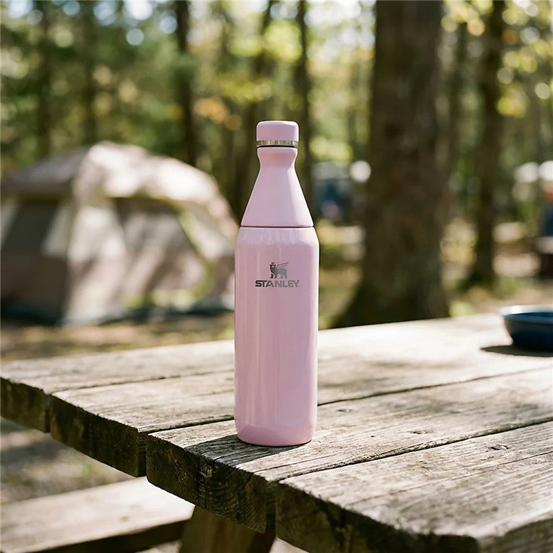 Stanley The All Day Slim Bottle 20 oz in Soft Orchid Gloss on a wooden picnic table in a forest setting.