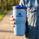 Blue Stanley The IceFlow™ Flip Straw 2.0 Tumbler (20 oz) held by a person in a denim jacket outdoors.