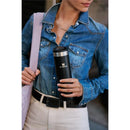 Stanley The Transit Fliptop Mug 20 oz in Rose Quartz held by a person in a denim shirt, with a black belt and a light bag.