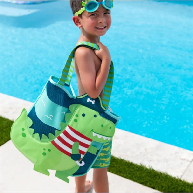 Boy smiling while carrying a shark-themed beach tote, wearing swim trunks and goggles, beside a swimming pool.