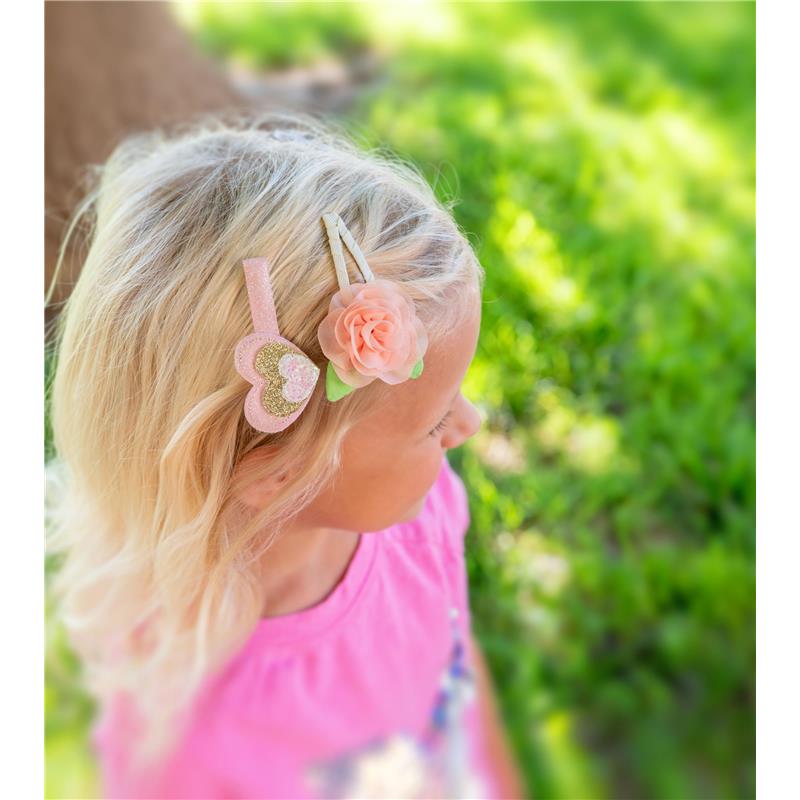 Hair clips featuring a heart and flower design are worn by a young girl with blonde hair, outdoors.