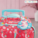 Luggage tag shaped like a mermaid attached to a bright pink suitcase decorated with mermaid and floral patterns.