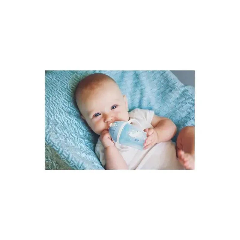 Baby holding a blue mermaid-themed straw cup while sitting on a light blue patterned cushion.