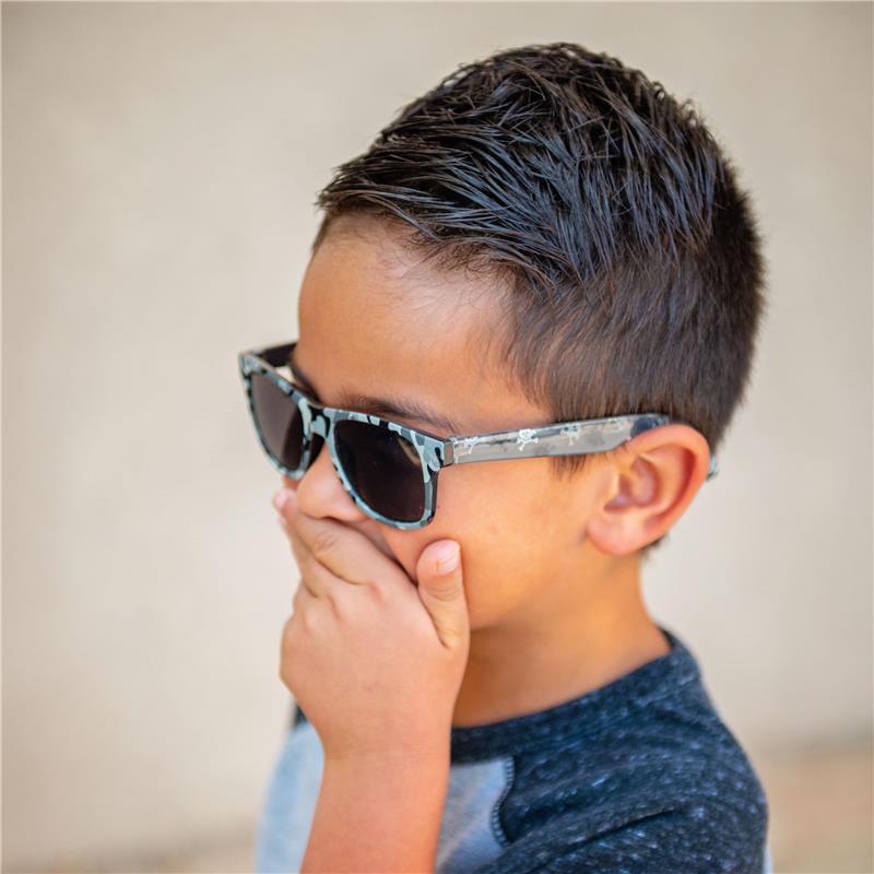 Boy with short hair wearing Stephen Joseph Flower sunglasses, covering his mouth with a hand, against a neutral background.