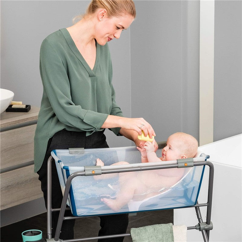 A woman bathing a baby in the Stokke Flexi Bath Stand, holding a sponge, in a modern bathroom setting.