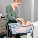 A woman bathing a baby in the Stokke Flexi Bath Stand, holding a sponge, in a modern bathroom setting.