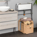 Stokke Flexi Bath Stand in grey, with a white folding bath attached, situated beside a wooden cabinet and storage boxes.