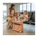 A woman helps a child use the Stokke Jetkids™ Bedbox™ in Midnight Grey, designed for travel convenience at an airport.