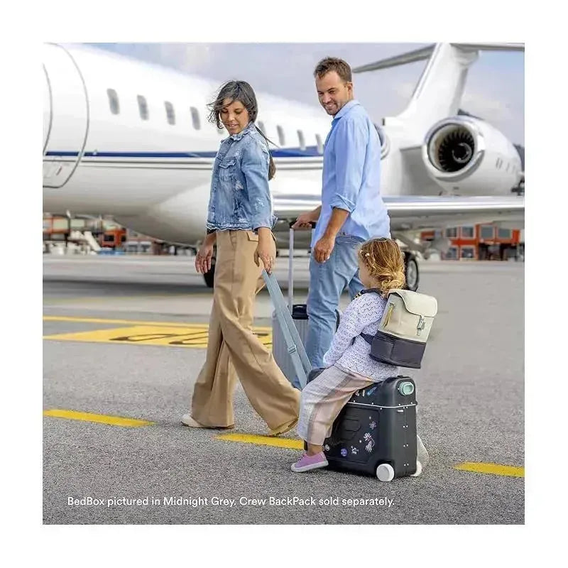 A family at an airport with a child sitting on a Stokke Jetkids™ Bedbox™ in Midnight Grey, ready for travel.