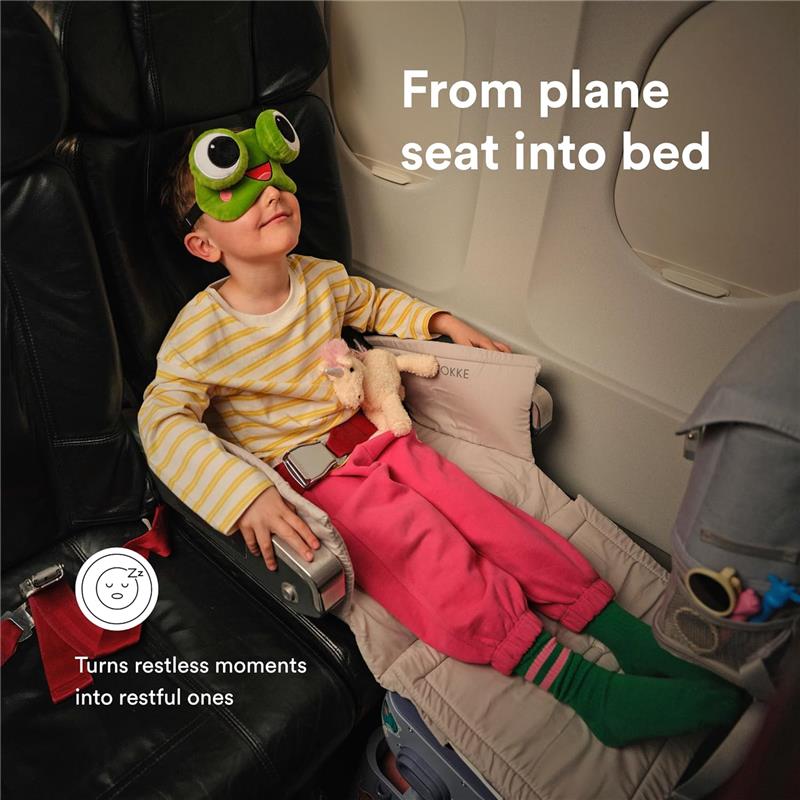 Stokke Jetkids™ Bedbox in Sea Green, transforming an airplane seat into a cozy bed for a resting child wearing frog eye mask.