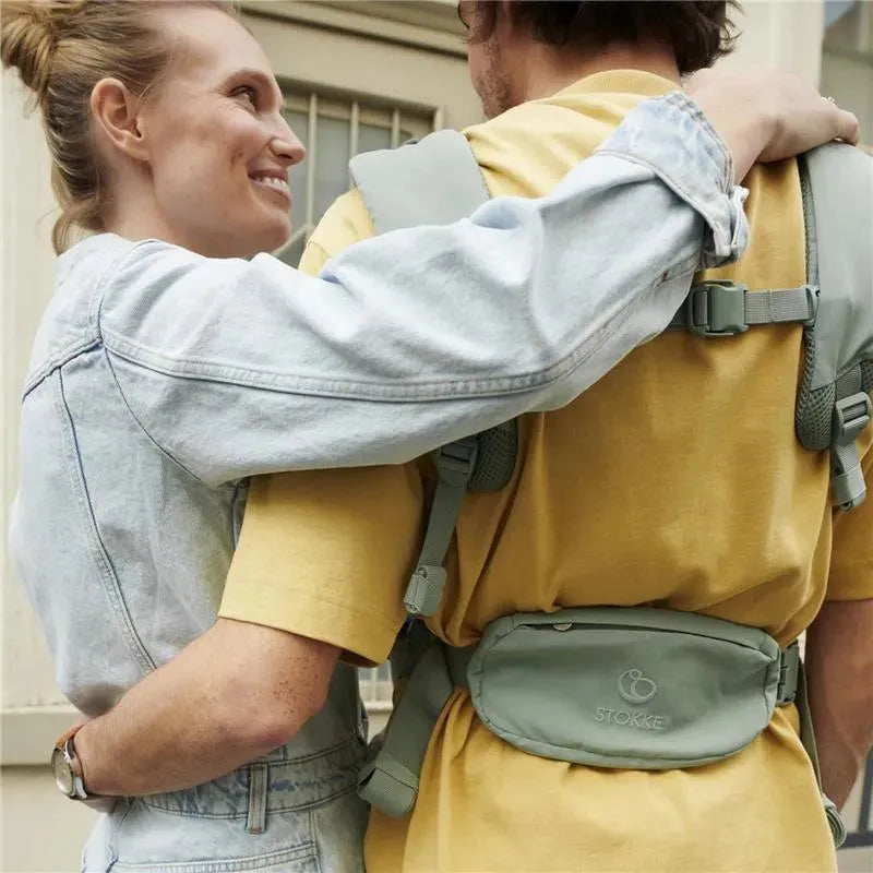 Couple embracing, featuring a man wearing a yellow shirt and a Stokke Limas Mesh carrier in Glacier Green.