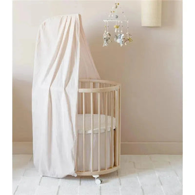 Stokke Sleepi crib with Pehr blush canopy, featuring a round wooden frame and a hanging mobile.