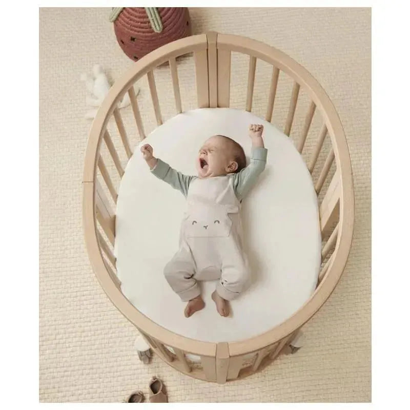Baby yawning in a Stokke Sleepi Mini Bundle V3 crib, wearing gray and white outfit, with a nursery backdrop.