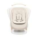 Stokke Yoga Baby Bouncer in light sand color, features a cushioned seat and secure harness on a wooden base.