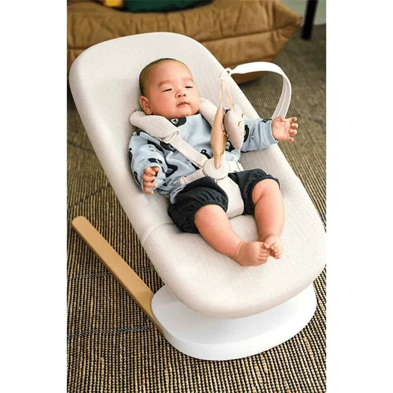 Stokke Yoga™ Baby Bouncer in Light Sand with a baby resting comfortably, secured with a harness, on a textured rug.