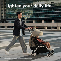 A man walks with a Yoyo stroller, featuring a child inside, against a modern city backdrop. The product is shown in black.