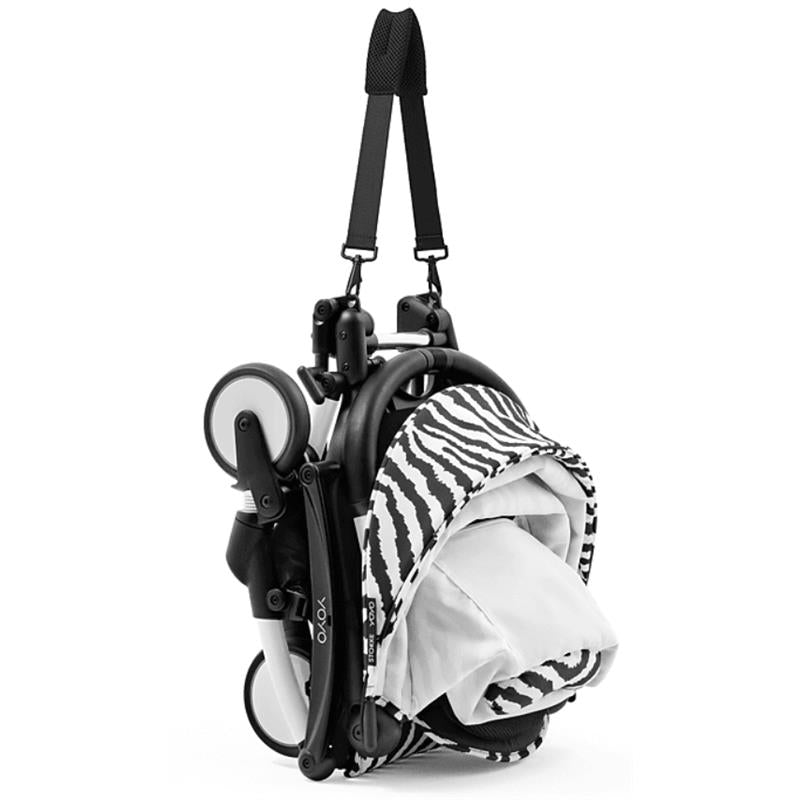 Stokke Yoyo³ stroller bundle in black and white with a zebra fabric, compactly folded and attached to a carrying strap.