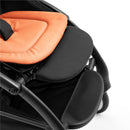 Stokke Yoyo5 Compact Stroller featuring a black frame and a peach-tinged seat pad, with a textured footrest visible.