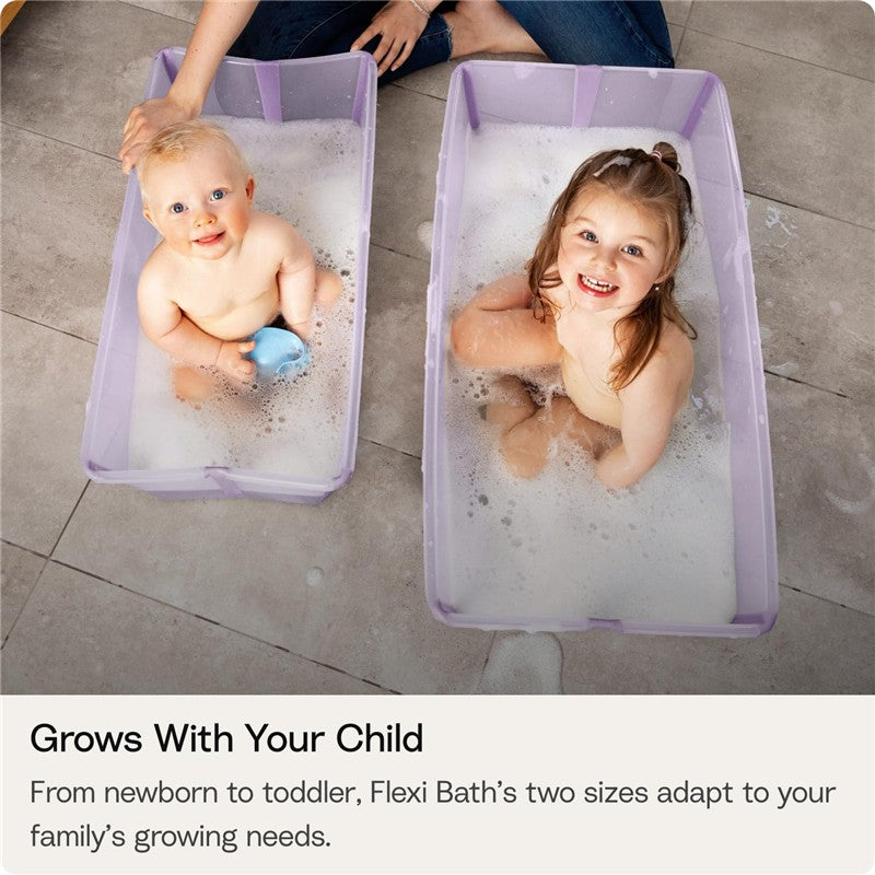 Two children, a baby and a young girl, are happily playing in the Stokke® Flexi Bath®Bundle in Ocean Blue, filled with bubbles.