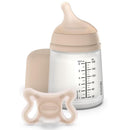 Suavinex Zero Zero Newborn Starter Set featuring a small anti-colic baby bottle and a pacifier, both in light beige.