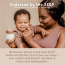 A smiling baby holding a Suavinex Zero Zero anti-colic baby bottle, while being embraced by a woman, highlighting oral comfort.