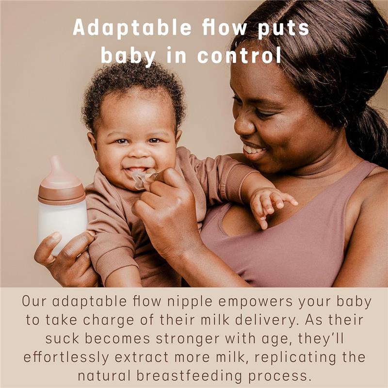Newborn baby smiling while holding a Suavinex anti-colic baby bottle with a pacifier, showcasing adaptable flow.