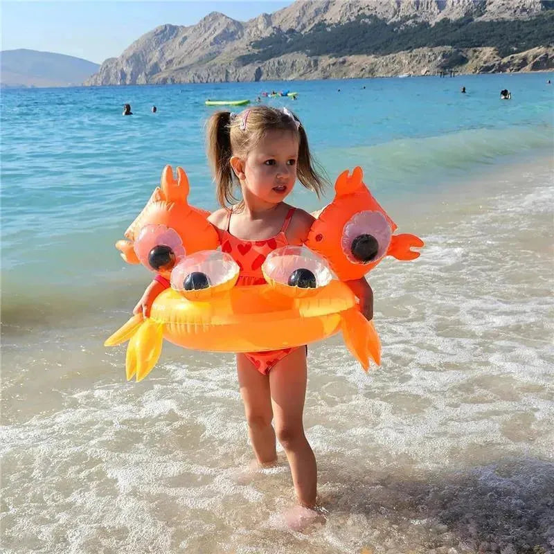 A girl in a red swimsuit walks in shallow water, wearing orange inflatable float bands shaped like a crab.