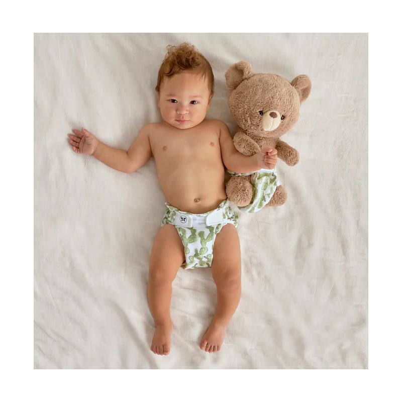 Infant wearing a Swaddle Designs Honest Cotton Muslin Hybrid reusable diaper cover with a cactus pattern, holding a teddy bear.