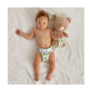 Infant wearing a Swaddle Designs Honest Cotton Muslin Hybrid reusable diaper cover with a cactus pattern, holding a teddy bear.
