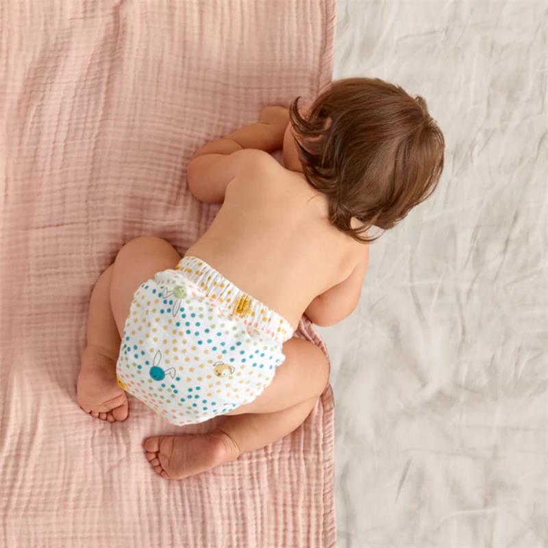 Reusable cloth diaper cover with colorful spots, worn by a baby lying on a soft, textured blanket.