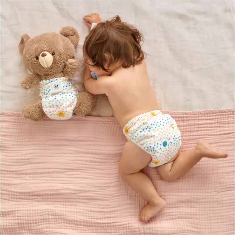 Reusable cloth diaper cover with spotted design, worn by a child lying beside a teddy bear also dressed in a matching diaper.