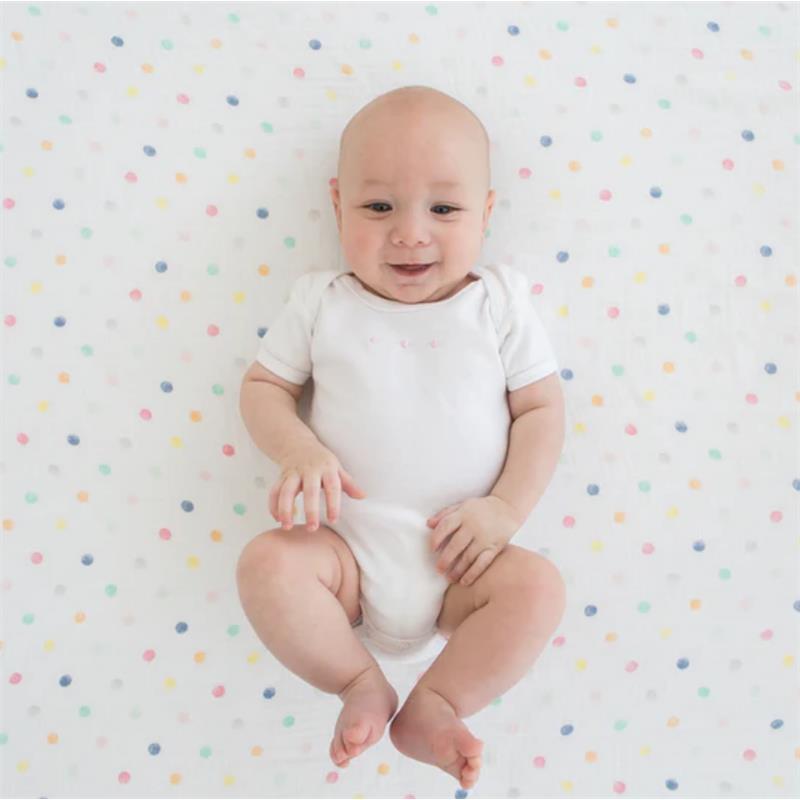 Baby smiling while lying on a colorful, polka-dotted muslin swaddle blanket.