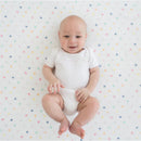 Baby smiling while lying on a colorful, polka-dotted muslin swaddle blanket.